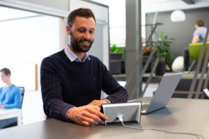 Junger Mann arbeitet am Schreibtisch und schaut dabei auf seine Isa.