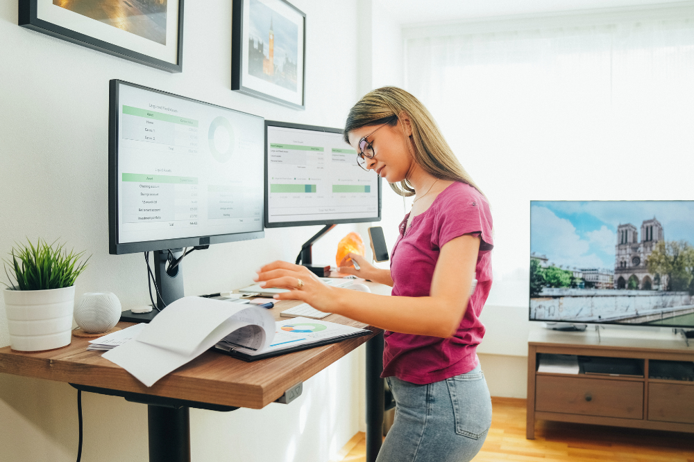 Mitarbeiterin im Homeoffice arbeitet im Stehen an einem höhenverstellbaren Schreibtisch.